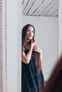 Candid portrait of sensual smiling asian girl young woman with dark long hair in black dress looking at mirror Royalty Free Stock Photo