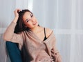 Candid portrait of sensual smiling asian girl young woman with dark long hair in cozy beige sweater sitting on blue vintage chair Royalty Free Stock Photo