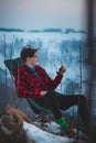 Candid portrait of a smiling teenager aged 15-20 of European descent sitting on a chair and dressed in a plaid red-black shirt Royalty Free Stock Photo