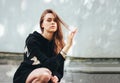 Candid portrait of young beautiful long hair unhappy girl fashion model hipster in black hoodie on wall background