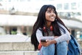 Young Indian woman sitting on steps with mobile phone and looking away Royalty Free Stock Photo