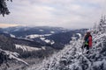 Candid portrait of young smiling man wearing colourful winter hiking jacket, warm-ups and white cap overlooking the snowy area of