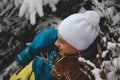 Candid portrait of a young smiling man wearing a colourful winter hiking jacket, warm-ups and a white cap during the winter season