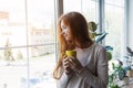 Portrait of young smiling red haired woman holding yellow coffee cup, enjoying morning coffee and new day Royalty Free Stock Photo