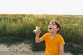 A boy in an orange T-shirt flies a kite in nature. Happy child