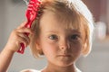 Candid serious thinking or sad young baby caucasian blonde girl with small scratch comb with hair brush at home Royalty Free Stock Photo