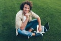 Candid shot of cheerful freelance man with curly hair using laptop for working outdoors, connected to free wireless, sitting on Royalty Free Stock Photo