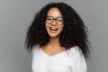 Candid shot of optimistic curly woman laughs positively, being in good mood, has healthy skin, looks through transparent glasses,