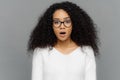 Candid shot of shocked beautiful woman in glasses with dark frizzy hair, keeps jaw dropped from amazement, being in stupor after Royalty Free Stock Photo