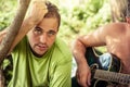 Candid young man with sincere look singing with guitar during outdoor camping party among foliage Royalty Free Stock Photo