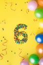 Candies number 6 with colorful balloons on yellow background. Concept for birthdays