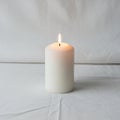 Candle is burning with a small flame placed on a plain white fabric Royalty Free Stock Photo