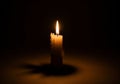 A candle burns in a dark setting. The flame emits a warm, yellow-orange glow, casting soft light Royalty Free Stock Photo