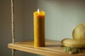 The candle burns during the day. A wax candle is on a shelf