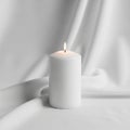 Candle burns with a steady flame, placed on a smooth, white fabric Royalty Free Stock Photo