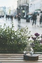 Candle in a candlestick on a wooden table. Raindrops on window glass, blurred unrecognizable people walk on road. View Royalty Free Stock Photo