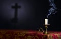 Candle on a dark background with the silhouette of the cross