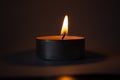 Candle on dark luxury night background. Black table, side view. Candles Burning at Night. Orange taper burning in focus,