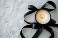 A candle encircled by a black ribbon, resting on a white table Royalty Free Stock Photo