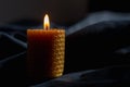 Candle with flame, orange wax burning candle on dark blue fabric background