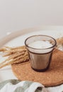 A candle in a glass beaker on a cotton napkin on a white table, next to it is a bouquet of dried flowers. Warm colors