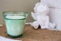 Candle in green glass vase with white ceramic angel. New candle and cute angel statue. Aromatherapy concept.