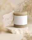 Candle with label on beige stone near dried pampas grass close up, copy space, mock up