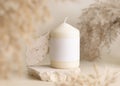 Candle with label on beige stone near dried pampas grass close up, copy space, mock up