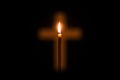 Candle is glowing through hole in shape of Christian cross