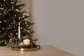 Candle lights burning on table, blurred Christmas tree with shining lights and empty neutral beige wall background. Minimal Royalty Free Stock Photo