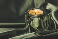 A candle in a metal holder on a dark olive green silk tablecloth. Stylish decor. Royalty Free Stock Photo