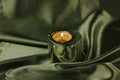 A candle in a metal holder on a dark olive green silk tablecloth. Stylish decor. Royalty Free Stock Photo