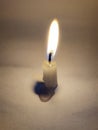 A candle placed on a white surface glows against the darkness, shedding light
