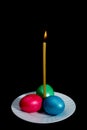 Candle, three Easter eggs on a plate, isolated on black background Royalty Free Stock Photo