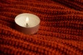 Candle stands on brown knitted cloth. Ginger color knitted cloth. Warm colors photo. Autumn and winter. Cold season concept. Cozy