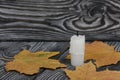 A candle stub on brushed pine boards. Dried maple leaves all around