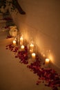 Candle surrounded by red rose petals with dreamy reflection
