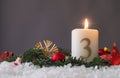 Candle of the third Advent burns, fir branches and Christmas tree balls in the snow