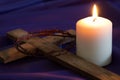 Candle and wooden cross with thorns on violet fabric background, concept Royalty Free Stock Photo