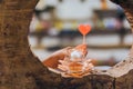 Candlelight in small glass cup with blured image of a red heart shaped candle in a woman`s hand.