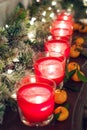 Candles in glass candlesticks stand on a shelf with a luminous garland and tangerines