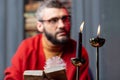 Bearded diviner sitting near burning candles and reading ancient book Royalty Free Stock Photo