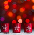 Candles standing in snow with defocussed fairy lights, red bokeh in the background, Festive Christmas background