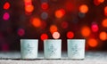 Candles standing in snow with defocussed fairy lights, red bokeh in the background, Festive Christmas background Royalty Free Stock Photo