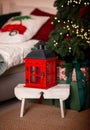 A candlestick in the form of a red retro lantern stands on a stool near the Christmas tree. Royalty Free Stock Photo