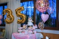 Candy bar large table with tasty sweets near window. Celebrating thirty-five years with two tier white cake with pink roses. Happy