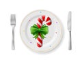 Candy cane is on white plate with fork and knife, top view
