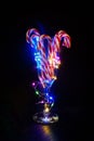 Candy canes in glass goblet with glowing garland on dark background