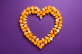 candy corn frame in a shape of heart on purple background for Halloween