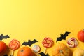 Candy, decorative bats and pumpkins on yellow background